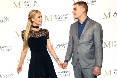 Paris Hilton, wearing black and Chris Zylka, wearing a gray suit holding hands at an event