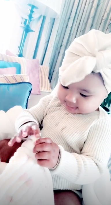 True Thompson sitting on Khloe's lap, wearing white