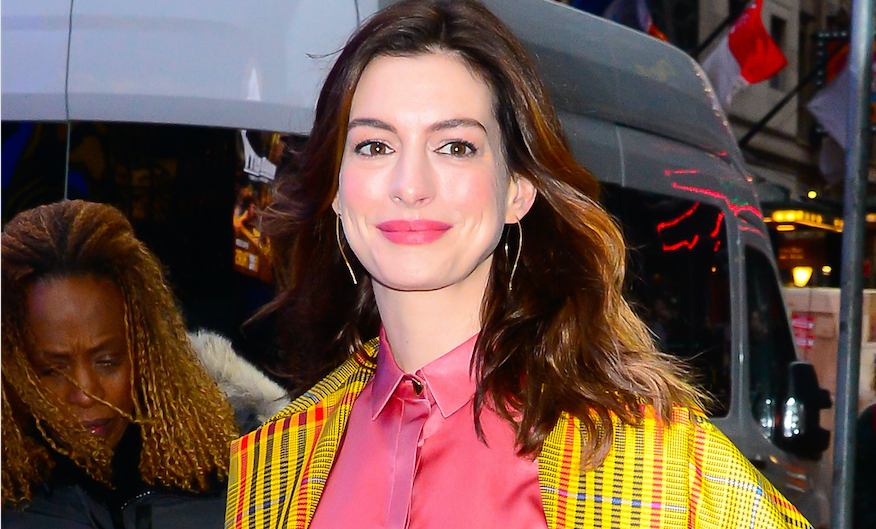 Anne Hathaway walking in NYC wearing a yellow plaid coat and coral dress