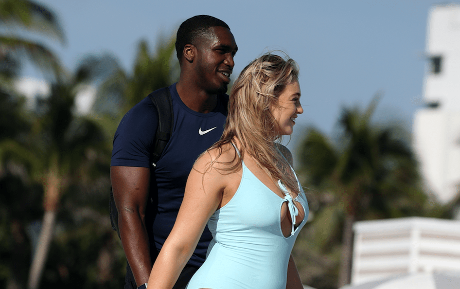 Iskra Lawrence walking with her boyfriend on the beach while wearing a blue bathing suit
