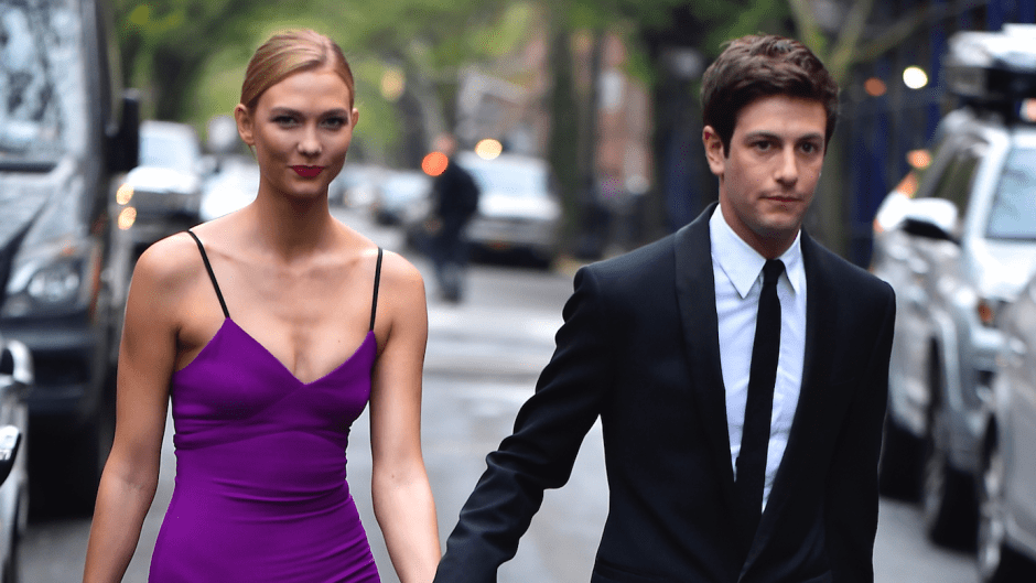 Karlie Kloss and husband Joshua Kushner walking down the street and holding hands, Karlie is wearing a purple dress and Joshua is wearing a black tuxedo