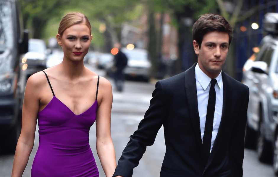 Karlie Kloss and husband Joshua Kushner walking down the street and holding hands, Karlie is wearing a purple dress and Joshua is wearing a black tuxedo