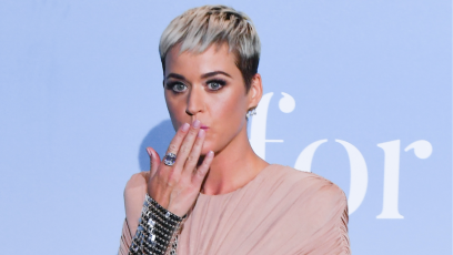 Katy Perry posing in a pink dress with her hand covering her mouth in shock