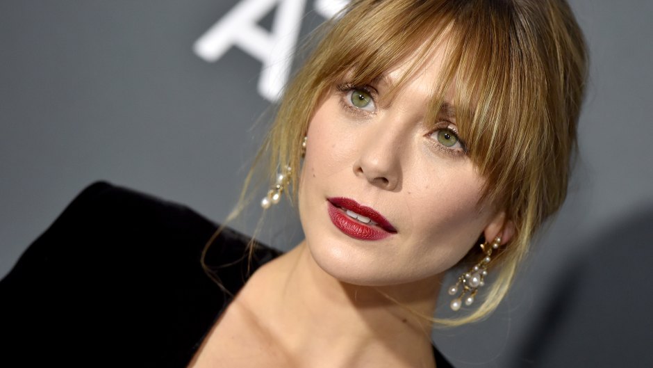 A zoomed in shot of Elizabeth Olsen wearing red lipstick, a black dress and gold earrings