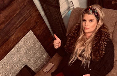 Jessica Simpson pregnant and lounging on a couch giving a thumbs up
