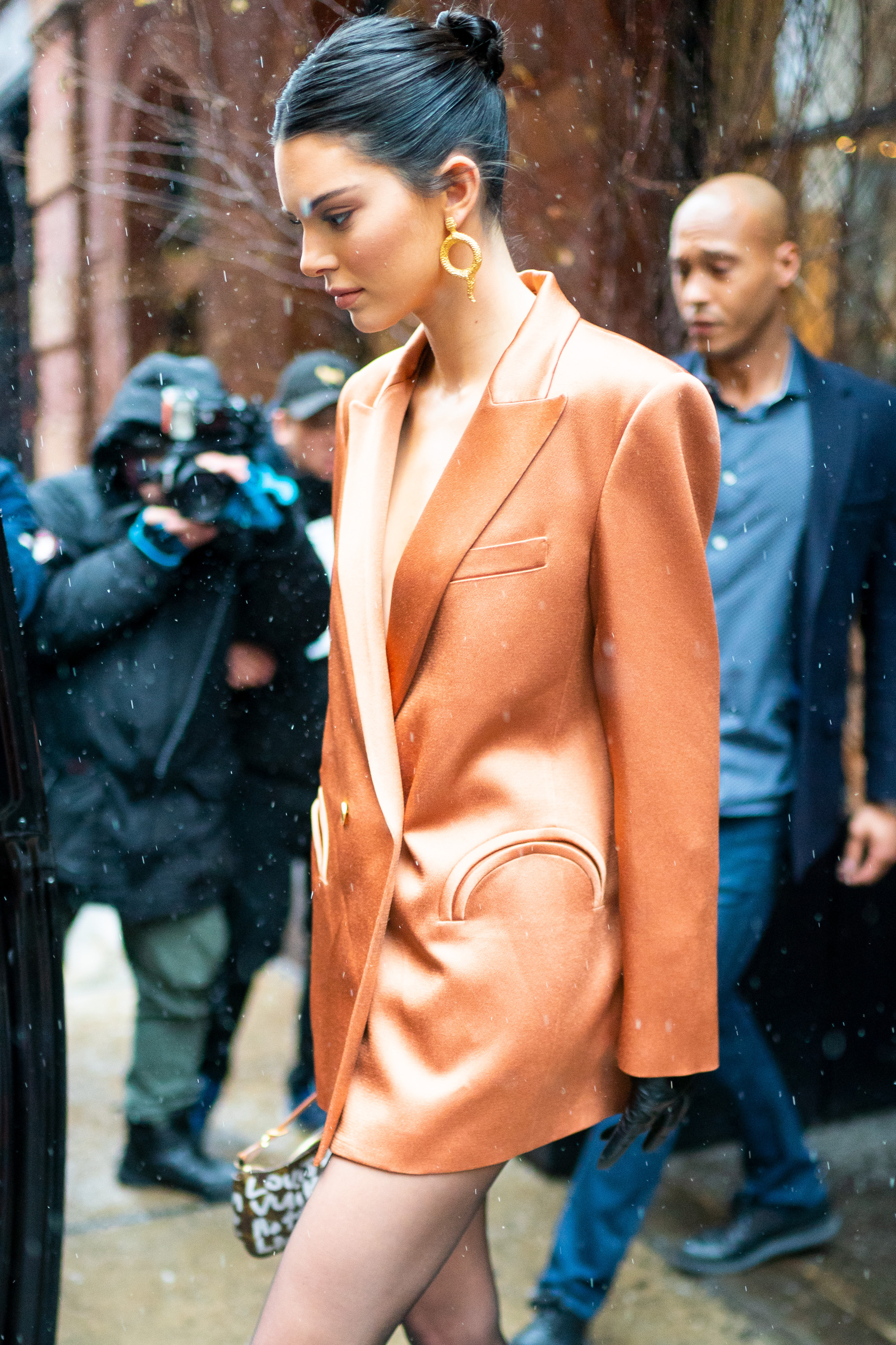 Kendall Jenner walking in NYC wearing an orange dress with black stockings and matching heels