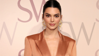 Kendall Jenner posing wearing an orange jacket with her hair up and gold earrings