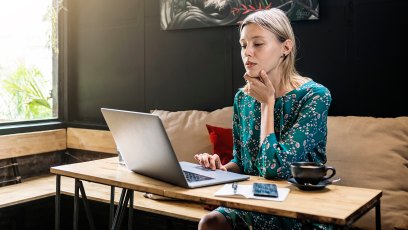 young woman with green dress sitting in café working on her laptop