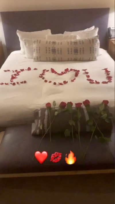 A picture of a white bed with rose petals that spell out "I love you."