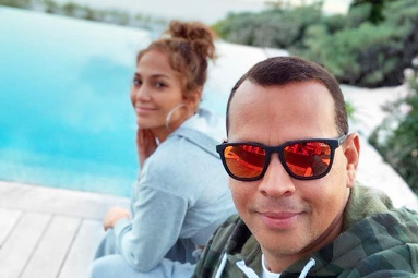 Alex Rodriguez and Jennifer Lopez taking a selfie next to a pool.