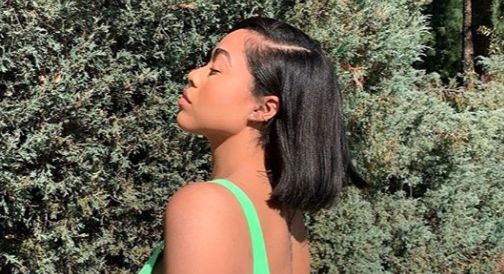 Jordyn Woods posing in a lime green bikini with short, black hair.