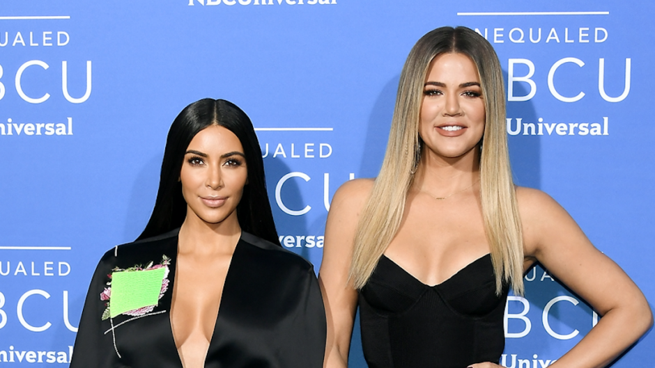 Kim Kardashian and Khloe Kardashian posing in front of a blue backdrop wearing all black.
