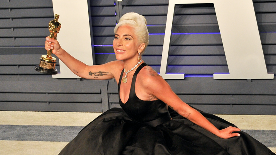 Lady Gaga kneeling on the red carpet with her Oscar trophy in hand