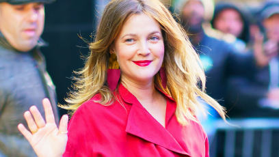 Drew Barrymore waving outside of Good Morning America NYC wearing a red pantsuit.