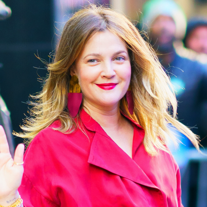 Drew Barrymore waving outside of Good Morning America NYC wearing a red pantsuit.