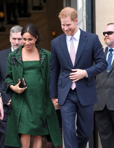 Meghan Markle wears green dress and coat with her hair up and Prince Harry holds her hand in a blue suit