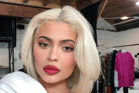 Kylie Jenner posing for a selfie with blonde hair and red lipstick.