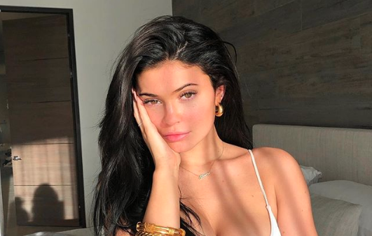 Kylie Jenner posing for a picture in the sunlight with her hand on her face.