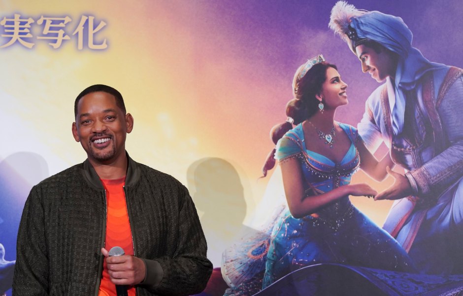 Will Smith Wearing an Orange Shirt In Front of Aladdin Sign