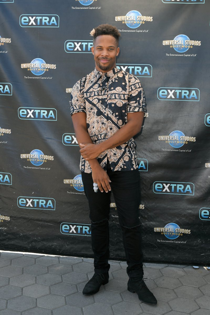 Bachelor Contestant Wills Reid Smiles on Extra Red Carpet in Patterned Shirt and Black Pants Holding His Right Arm