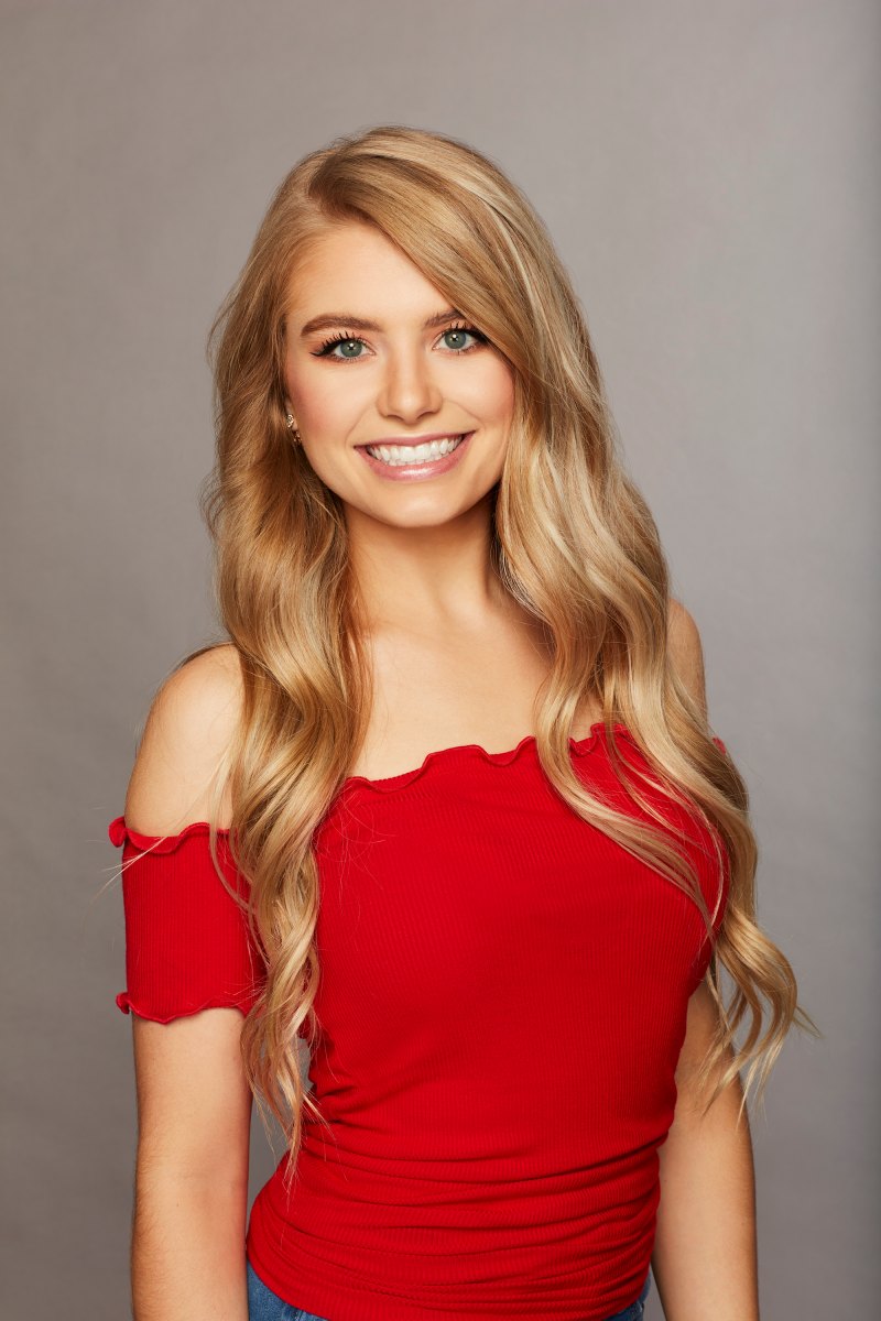 Bachelor Contestant Demi Burnett Stands Smiling in Her Cast Photo With Her Hair Curled and Wearing a Red Off the Should Top Bachelor in Paradise Cast List