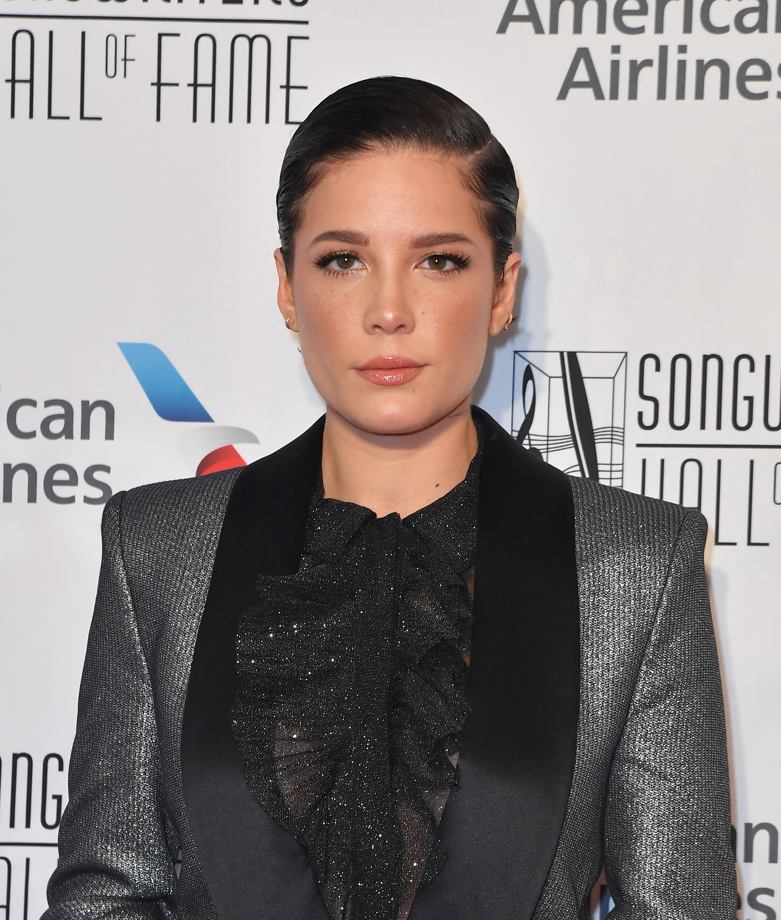 Halsey Smiles With Short Dark Hair Gelled Down and Silver Suit Coat and Blake Shimmery Blouse
