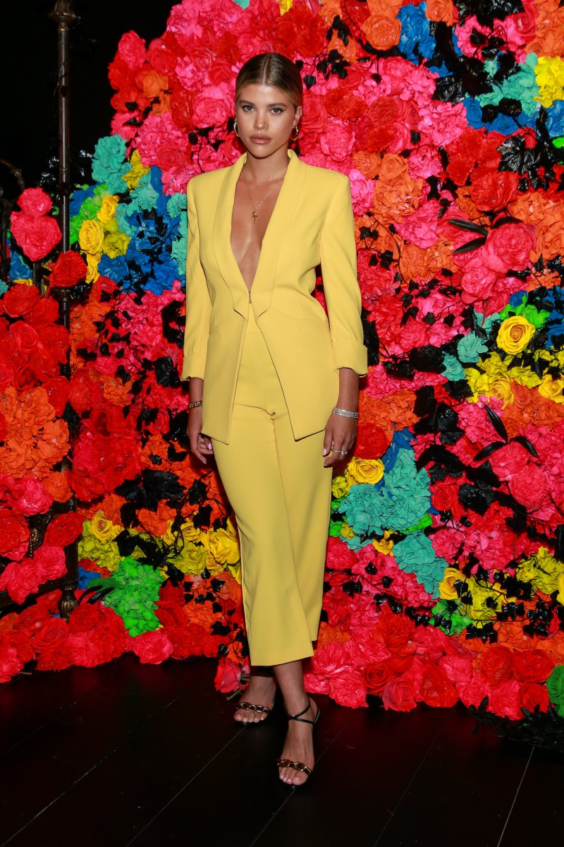 Sofia Richie Poses in a Yellow Suit Jacket With No Shirt and Yellow Pants and Strappy Heels Against a Rainbow Wall