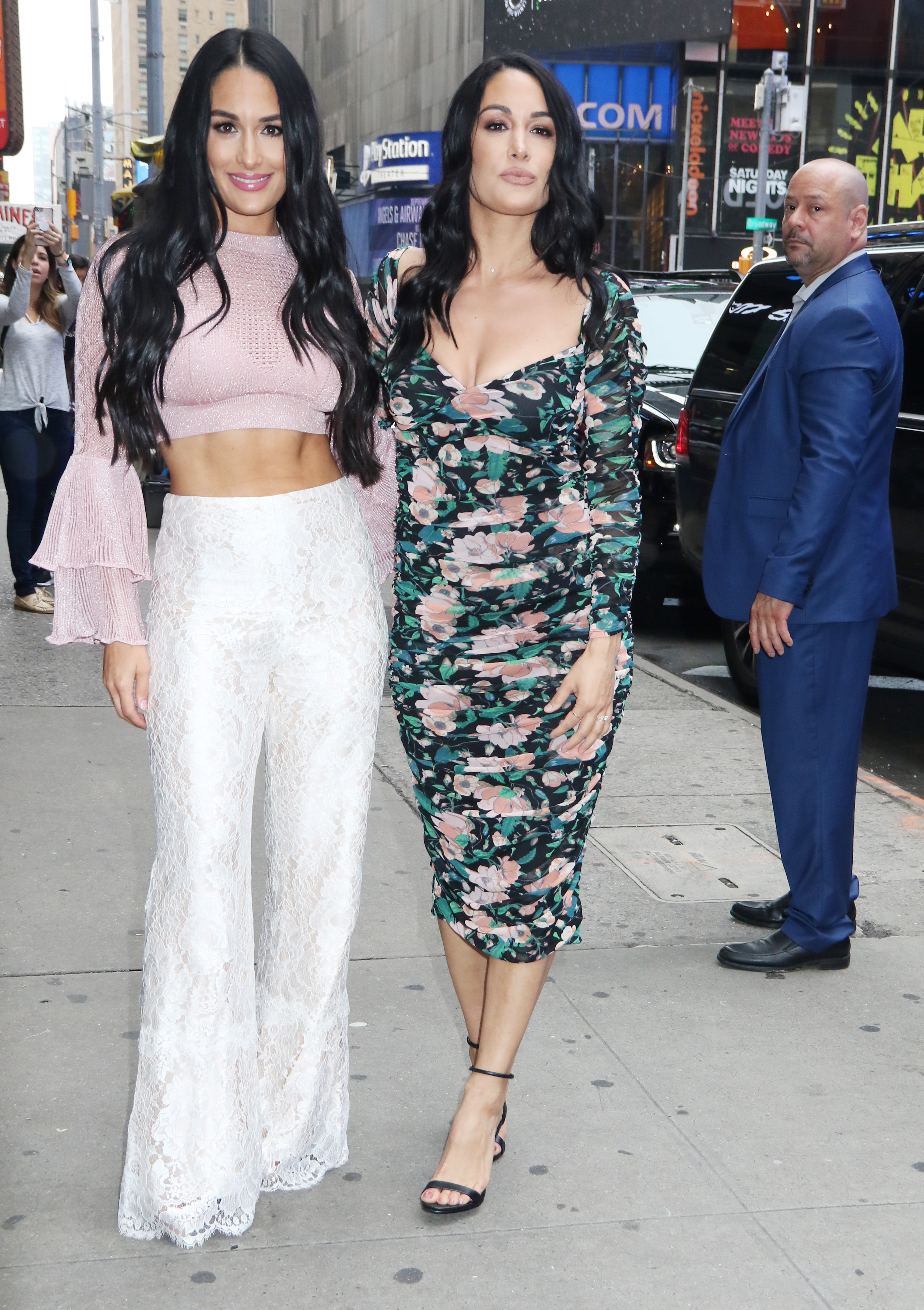 Nikki Bella in a Pink Crop Top and White Lace Pants and Brie Bella in a Flowered Dress Stand Together in New York City