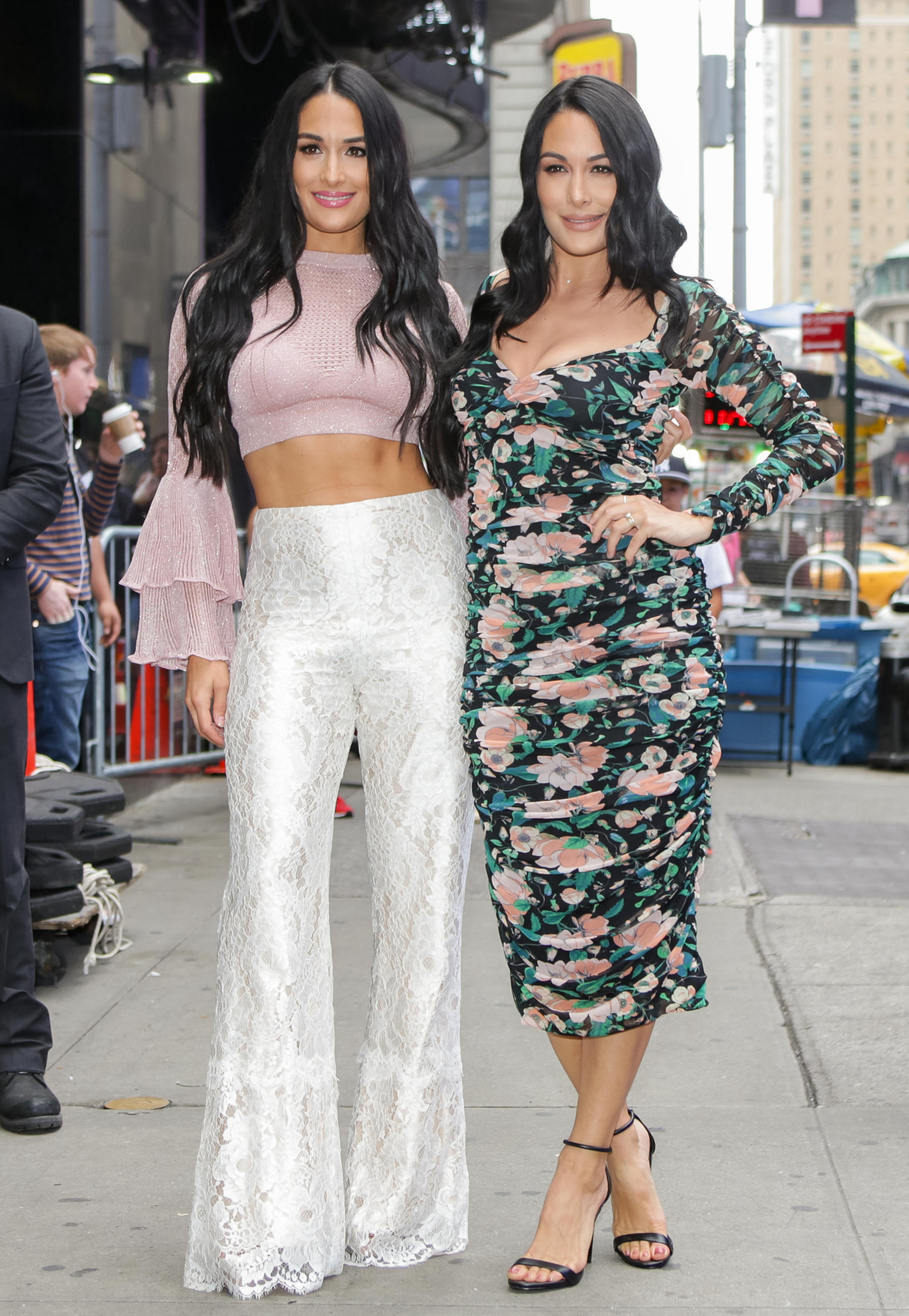 Nikki Bella in a Pink Crop Top and White Lace Pants and Brie Bella in a Flowered Dress Stand Together in New York City
