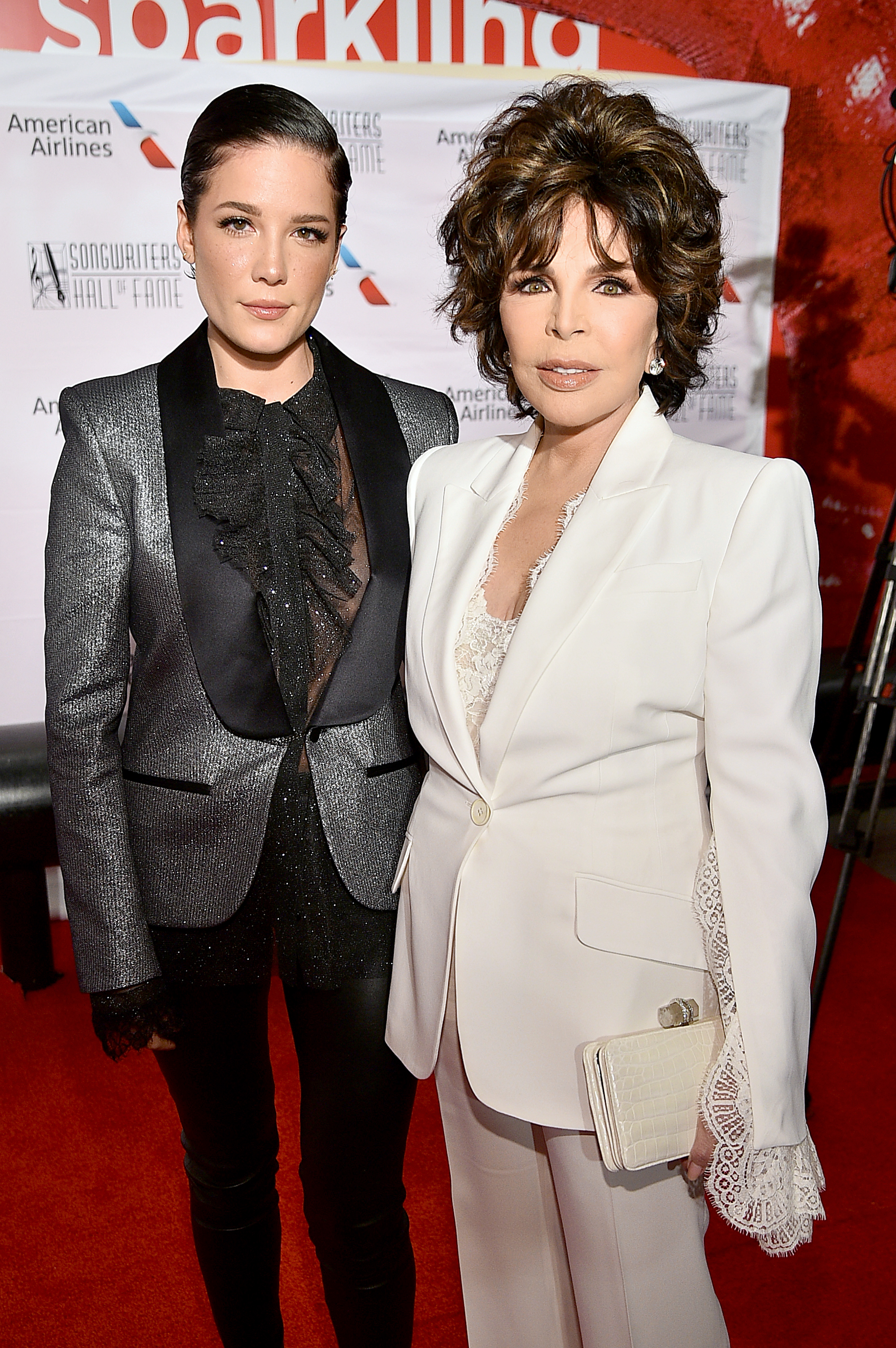 Halsey Poses in a Silver Tux Jacket See Through Black Blouse and Black Leather Pants Next to and Carole Bayer Sager in a White Suit Jacket With a White Blouse