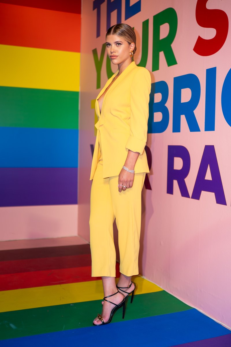 Sofia Richie Poses in a Yellow Suit Jacket With No Shirt and Yellow Pants and Strappy Heels Against a Rainbow Wall