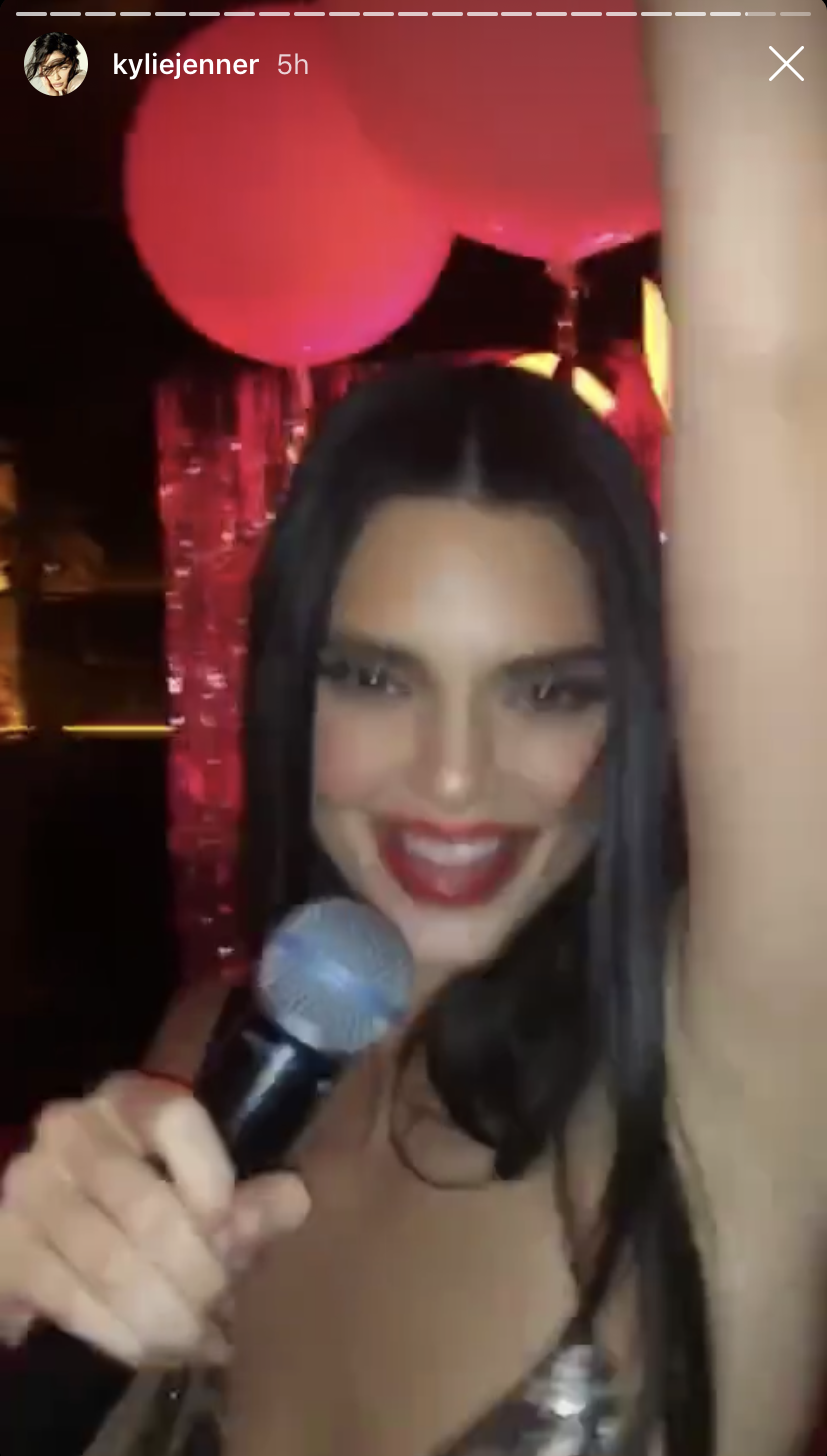 Kendall Jenner Smiling Holding a Microphone With One Arm Up