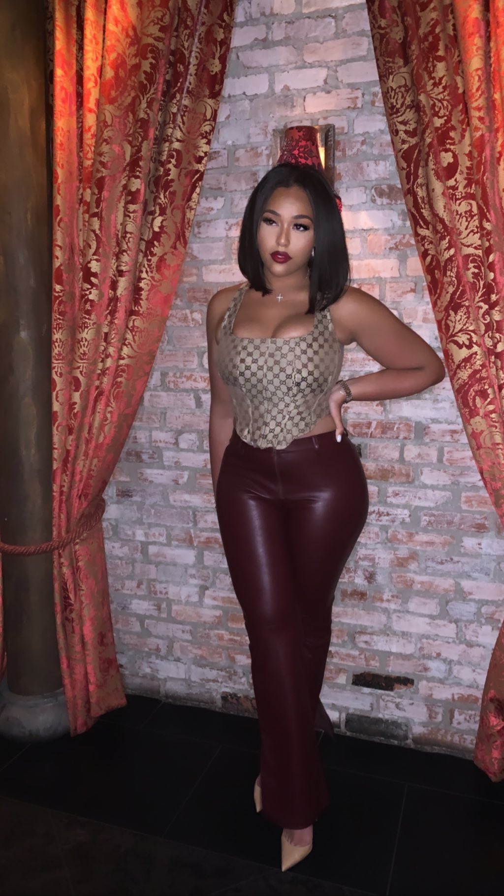 Jordyn Woods posing in a Gucci bustier, leather pants and nude heels