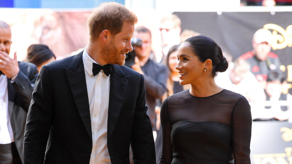 Prince Harry and Meghan Markle smiling at each other on the red carpet of The Lion King