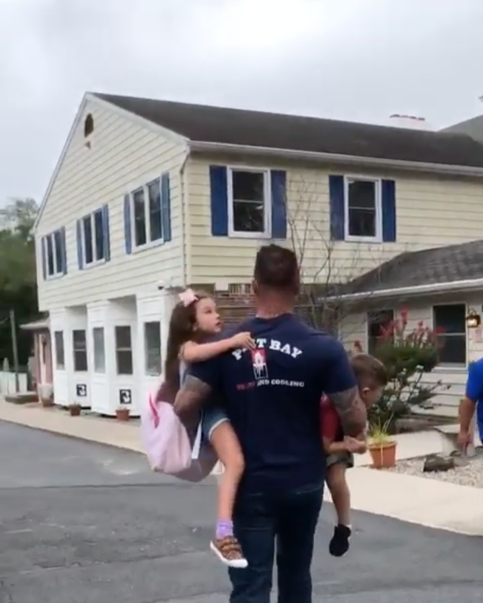 Roger Mathews carrying his two children into a school building