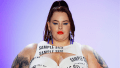 Tess Holliday walking the catwalk in a white dress with the words "sample size" printed on it