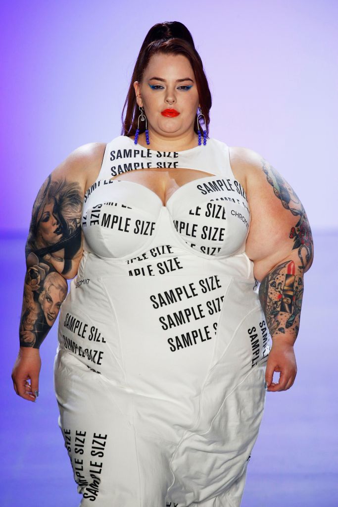 Tess Holliday walking the catwalk in a white dress with the words "sample size" printed on it