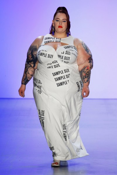 Tess Holliday walking the catwalk in a white dress with the words "sample size" printed on it