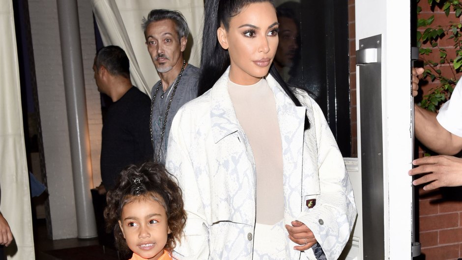 kim kardashian wears off-white top, white jacket and white pants and holds hands with daughter north who is wearing a peach kimono style dress
