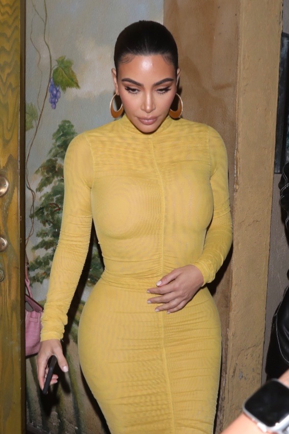 Kim Kardashian Wears Long Mustard Yellow Dress With Brown Hoop Earrings and Strappy Sandals and Pulled Back Hair