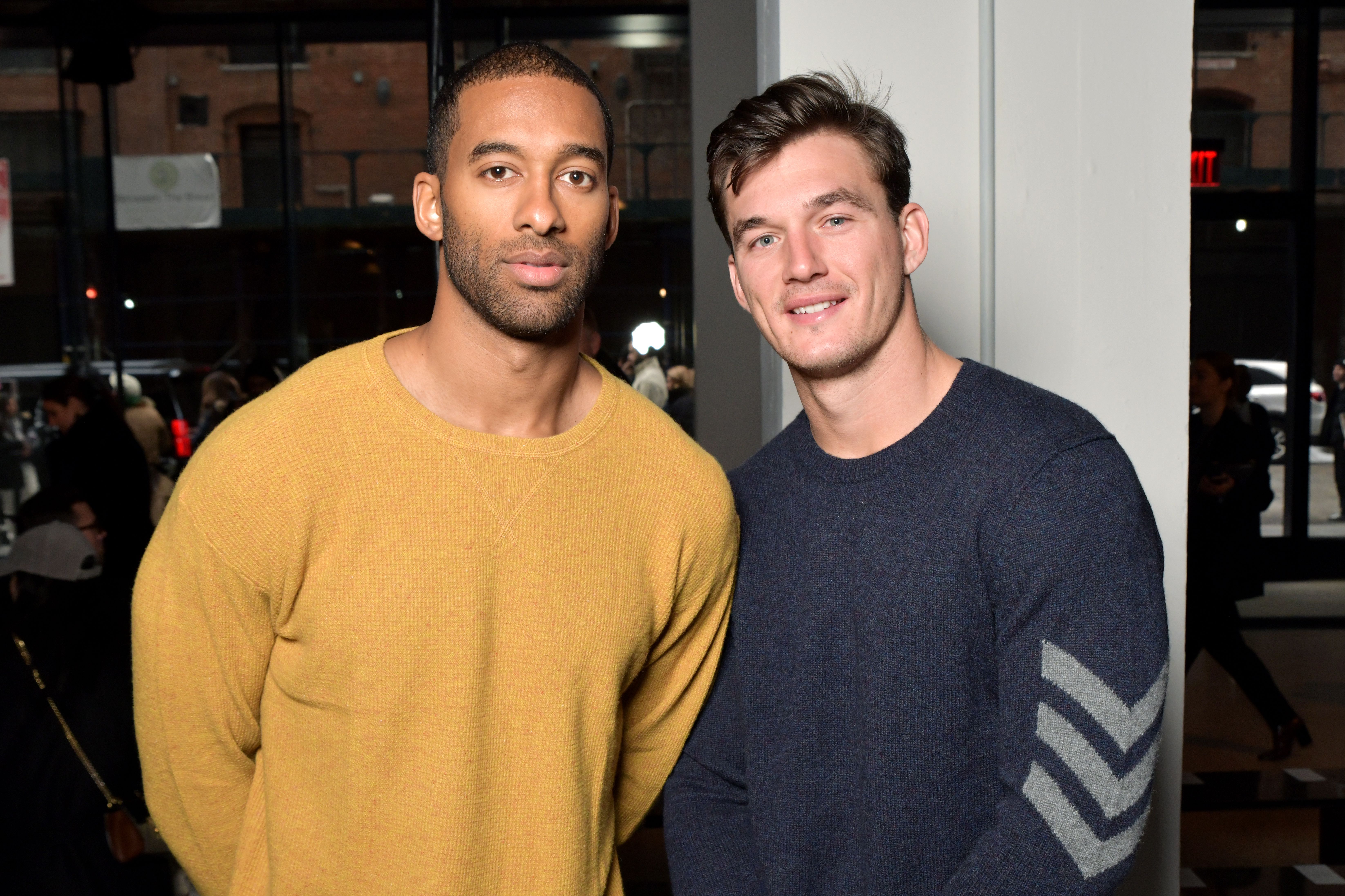 Tyler Cameron Smiles in Blue Sweater With Grey Arm Detailing With Friend Matt James in Yellow Sweater