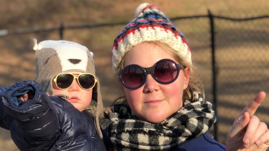 Amy Schumer Smiles Wearing Sunglasses a Hat and Scarf While Holding Son Gene in a Parka Hat and Sunglasses