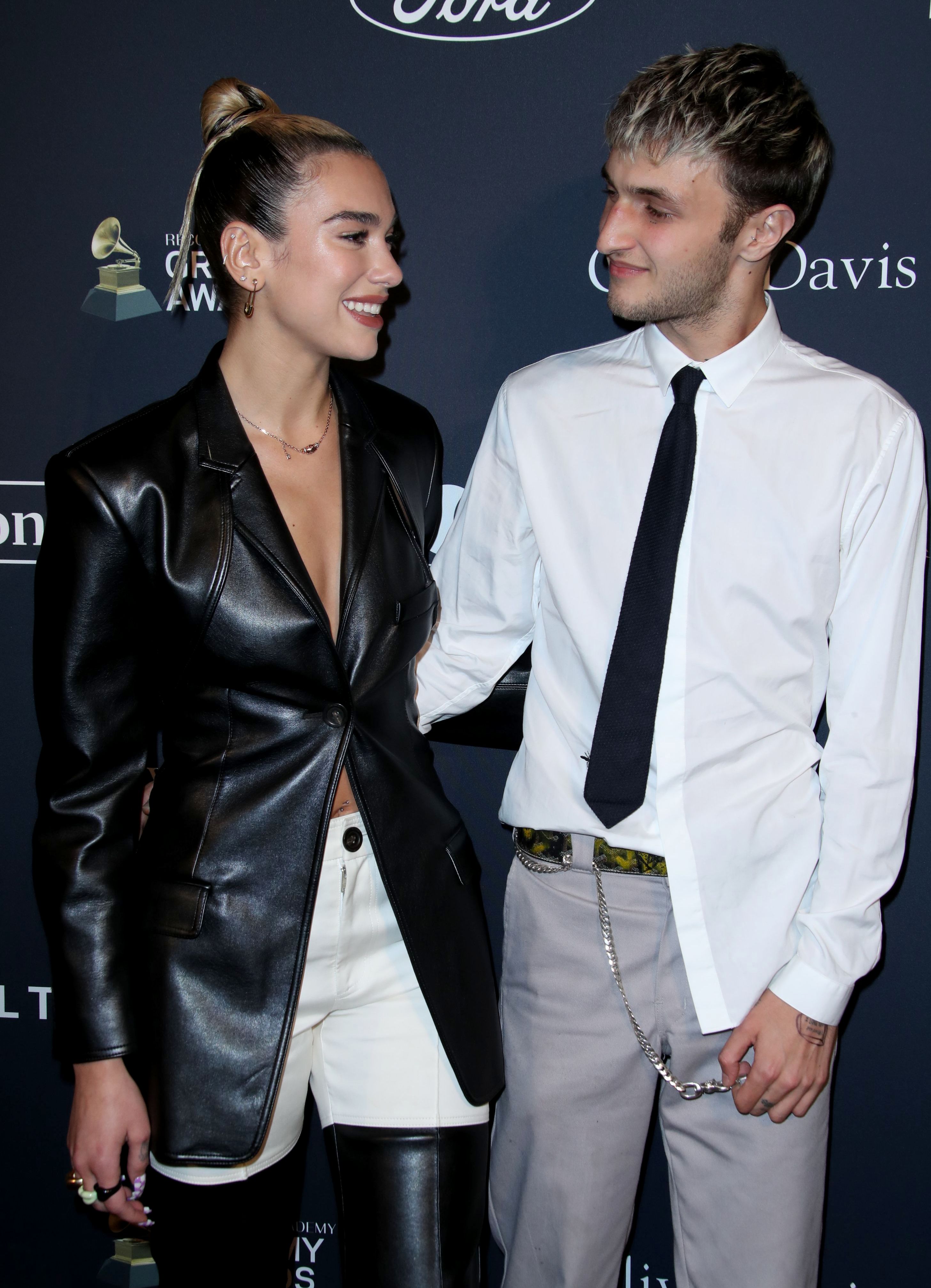 Dua Lipa Wears Leather Coat and White Pants and Laughs With Boyfriend Anwar Hadid in White Untucked Button Down Shirt and Grey Pants