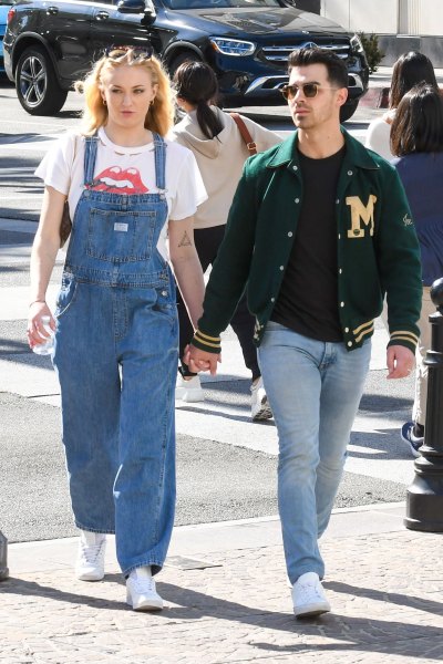 Sophie Turner Wears Jean Overalls and Graphic Tshirt and HOlds Hands With Husband Joe Jonas in Letterman Jacket and Jeans