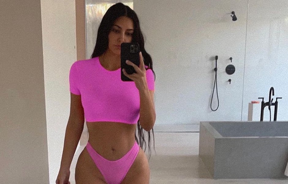 Kim Kardashian taking a selfie in her bathroom wearing a bright pink matching set.