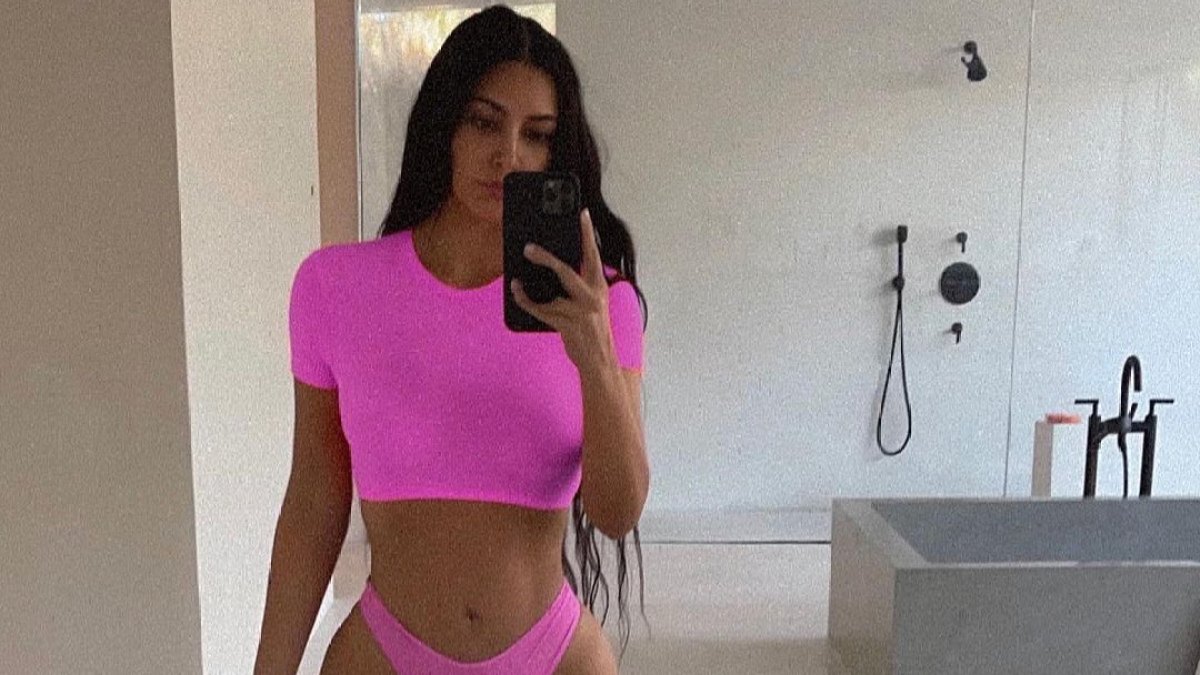 Kim Kardashian taking a selfie in her bathroom wearing a bright pink matching set.