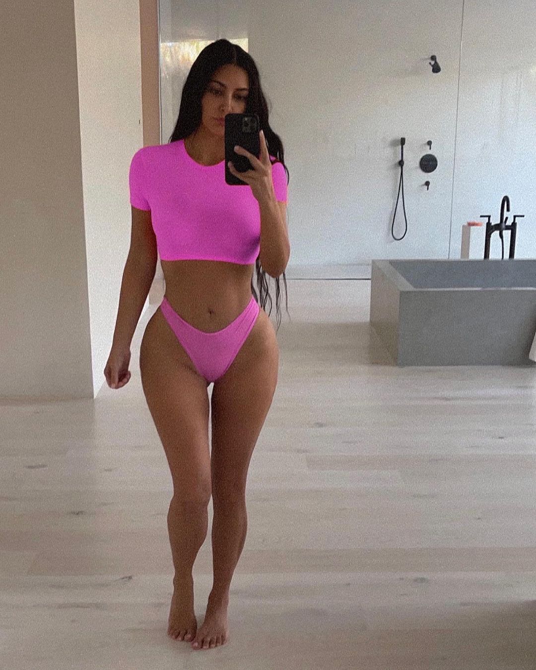 Kim Kardashian taking a selfie in her bathroom wearing a bright pink matching set.