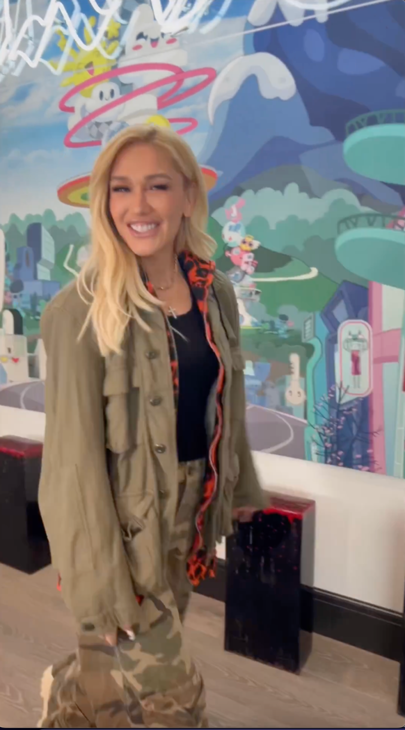 Gwen Stefani smiles in a green jacket and camo pants
