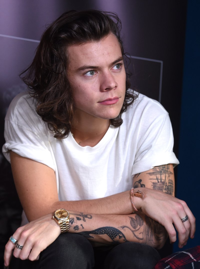 Harry Styles wearing a white T-shirt and sitting down with his arms crossed