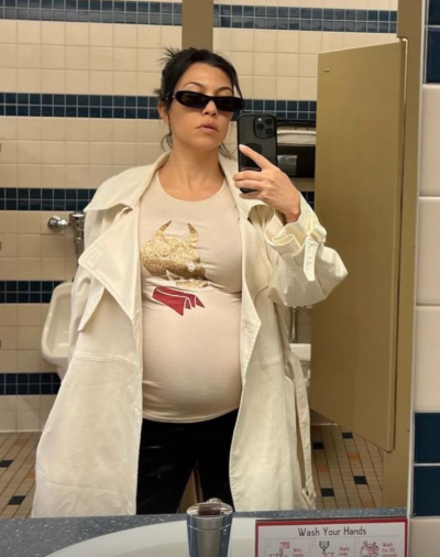 Kourtney Kardashian poses in a tight T-shirt that showcases her baby bump, black leggings and a white jacket